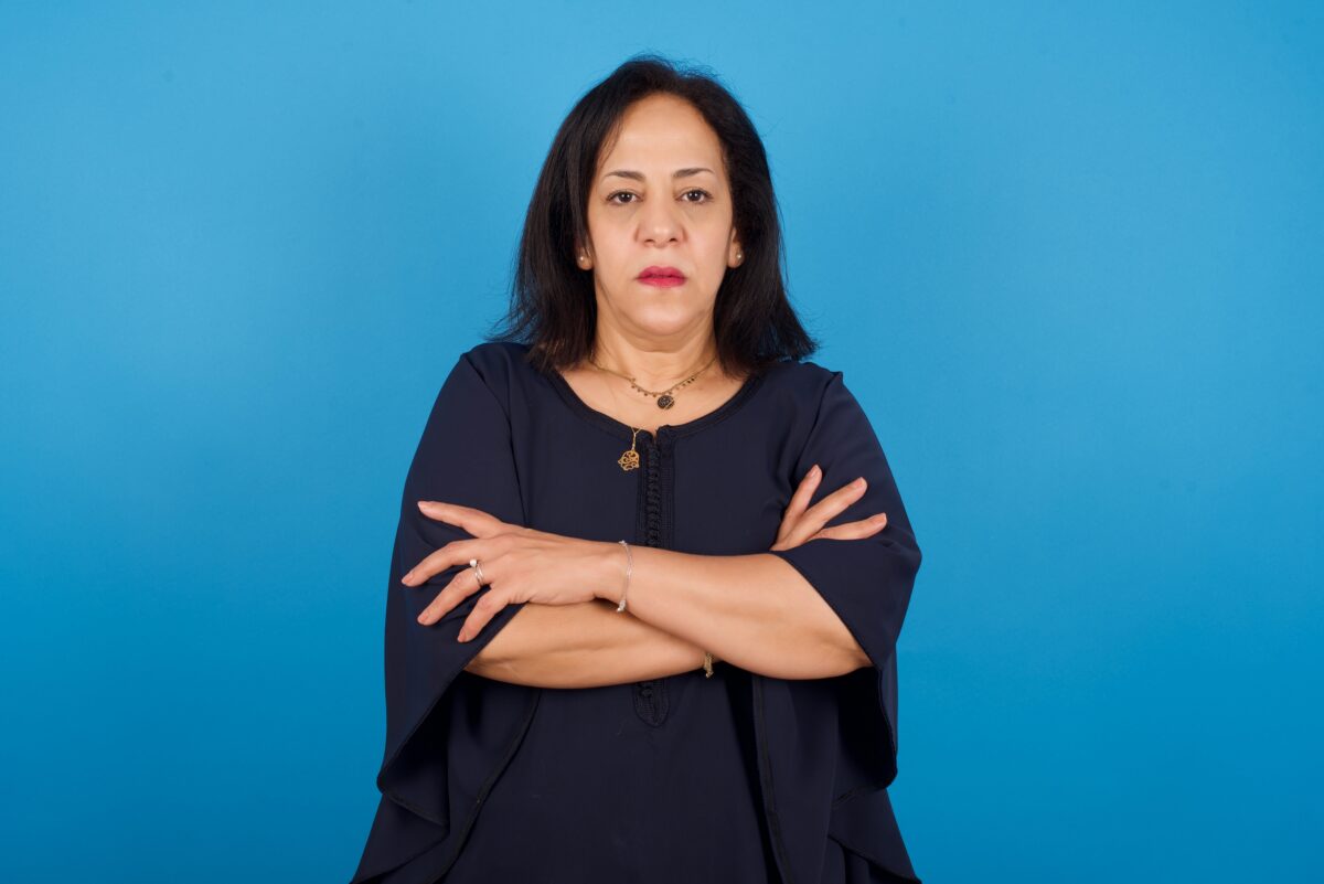 Confident woman standing with arms crossed against a blue background, symbolizing women empowerment and activism.