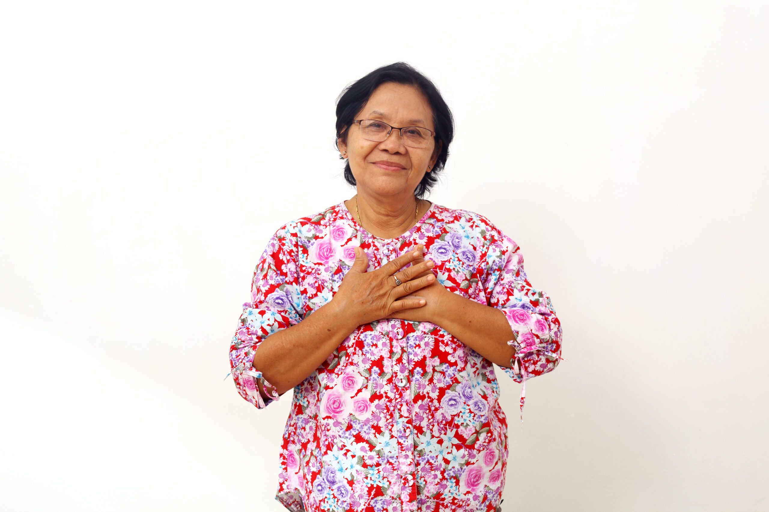 Portrait of happy asian senior woman standing while holding her chest. She feels relieved. Isolated
